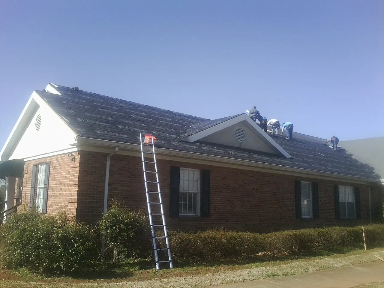 Crew tearing shingles off a brick ranch roof with a ladder set — Emergency Roof Repair work by our crew in Duncan Falls
