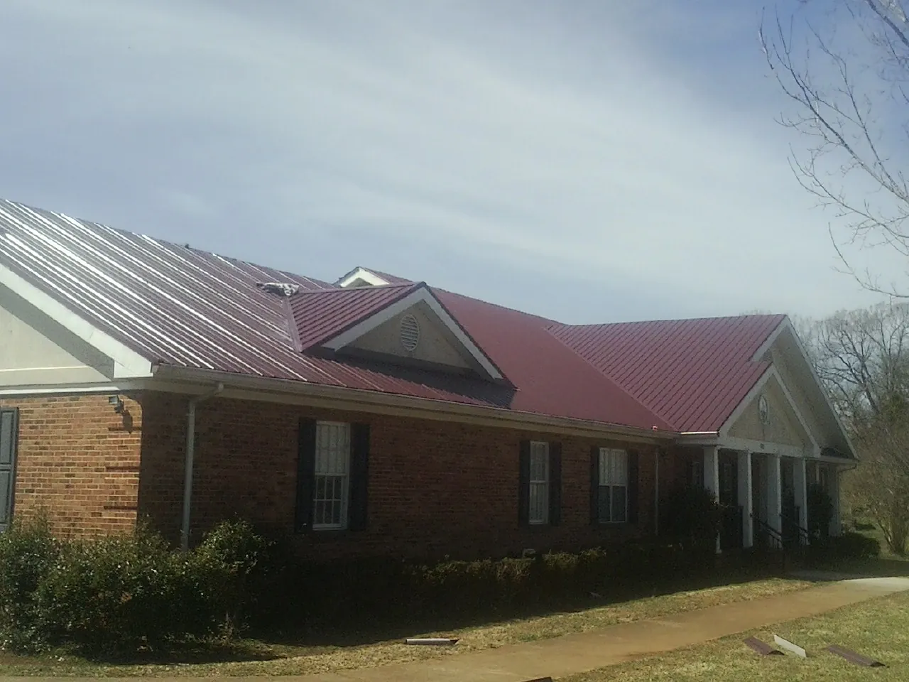 Red metal roof with gabled entries on a long brick building, from a Hail Damage Roof Repair job in Duncan Falls