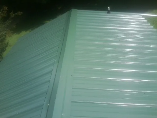 New green metal panels meeting at the ridge of a roof — Flat Roof Repair work by our crew in Duncan Falls