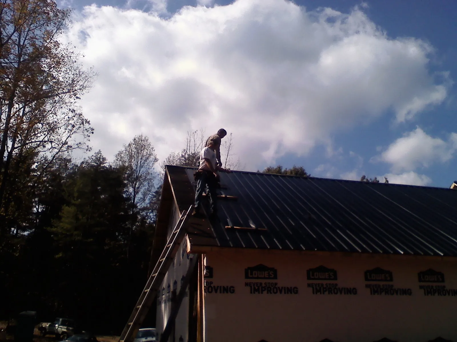 Roofer fastening dark metal panels high against a cloudy sky, from a Roof Inspection job in Duncan Falls