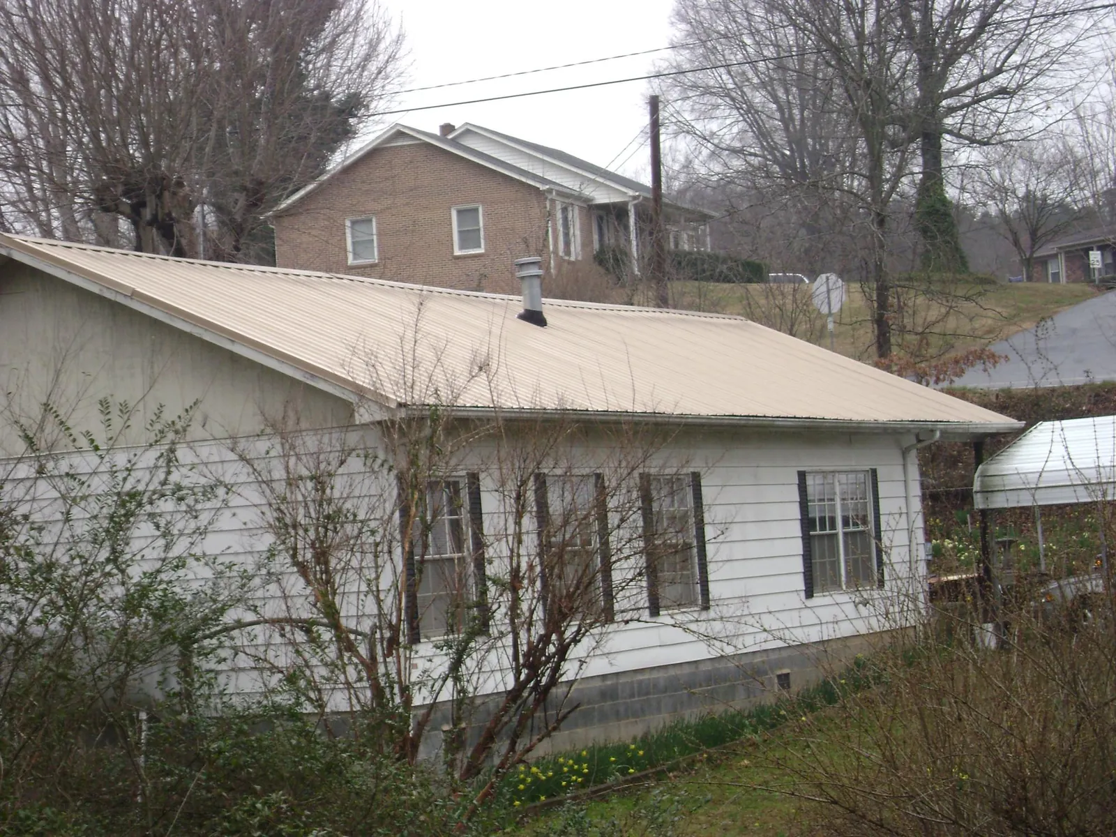 Tan metal roof on a white sided house set into a hillside — Commercial Roofing by Roofing Brothers in Duncan Falls