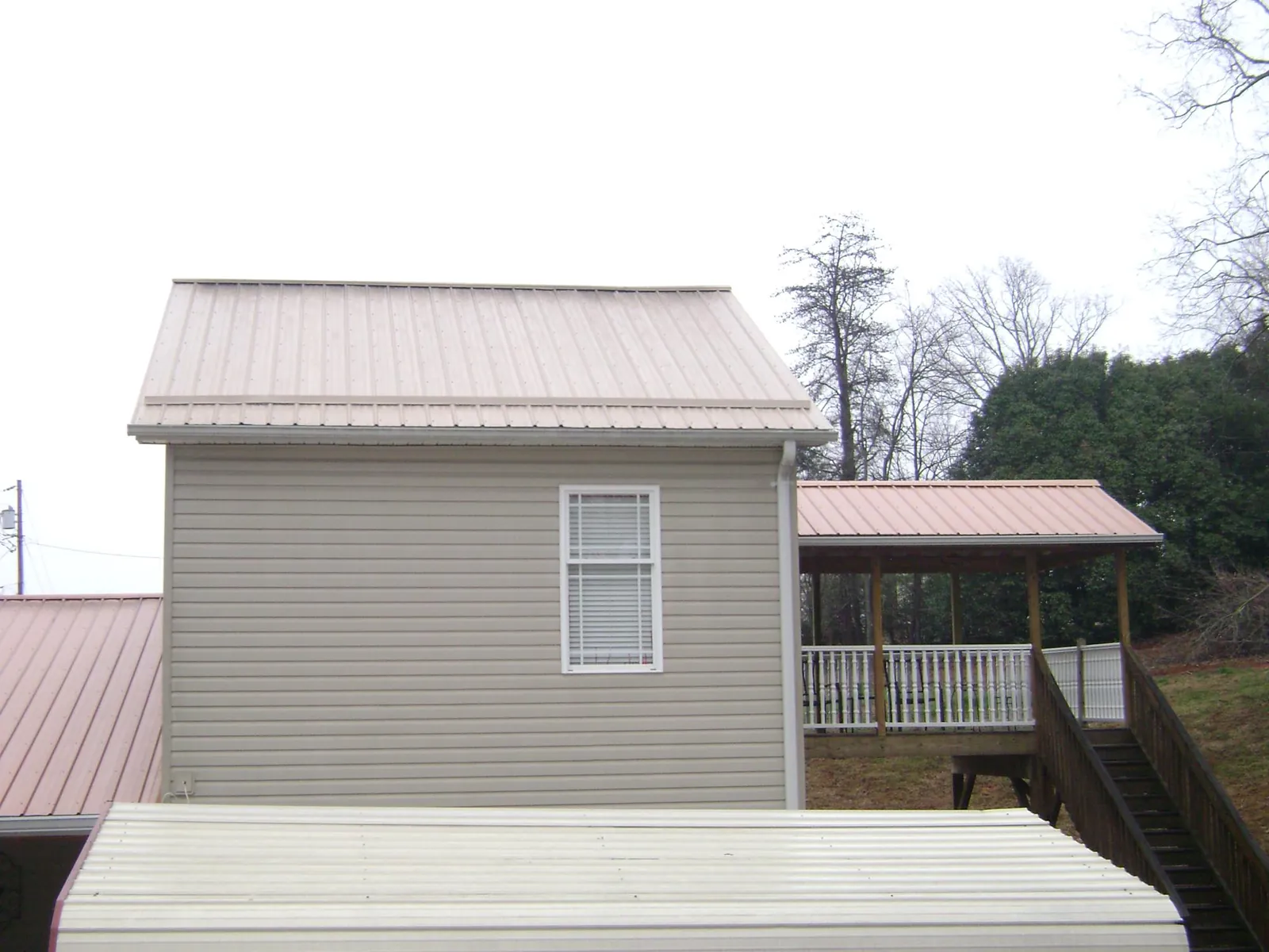 Tan metal roofs on a two story addition and attached porch, from a Roof Replacement job in Duncan Falls